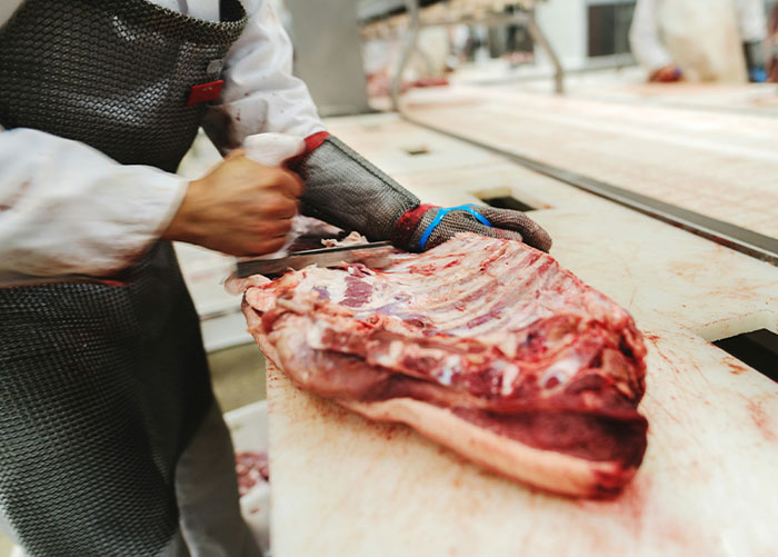 Butcher wearing protective gear cutting meat on a table, illustrating what professionals want the public to know about their jobs.
