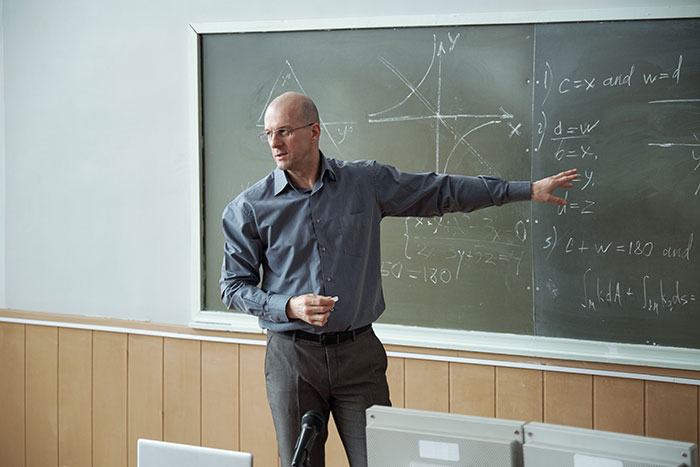 Professor explaining math concepts on chalkboard as students push back after phone rule enforcement in class without warning