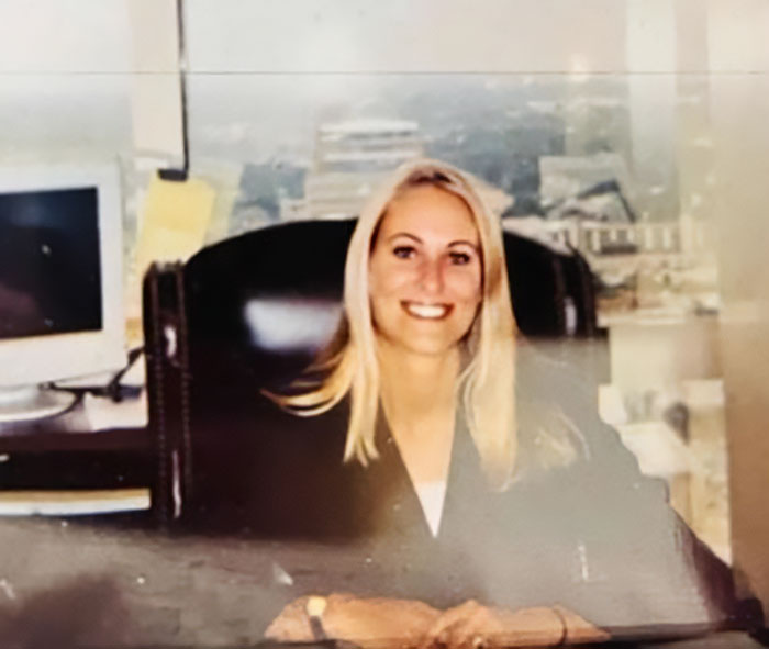 Smiling female lawyer seated at desk in office, professional environment, representing lawyer found deceased on transatlantic flight.