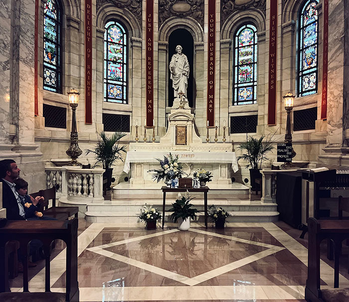 Interior of a church with stained glass windows and floral arrangements, evoking a solemn memorial atmosphere for a deceased lawyer.