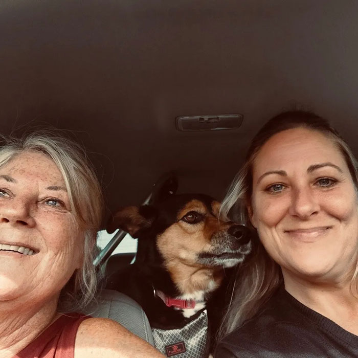 Two women smiling with a dog in a car, relating to a lawyer discovered deceased on transatlantic flight story.