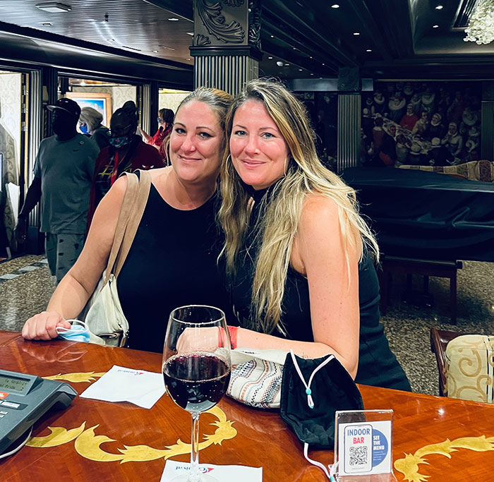 Two women sitting at a bar with wine, smiling and posing together, representing a casual social setting involving a lawyer.