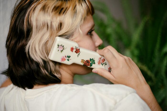 Person with two-toned hair holding a floral phone-shaped object, symbolizing DNA test results and surprising plot twists.