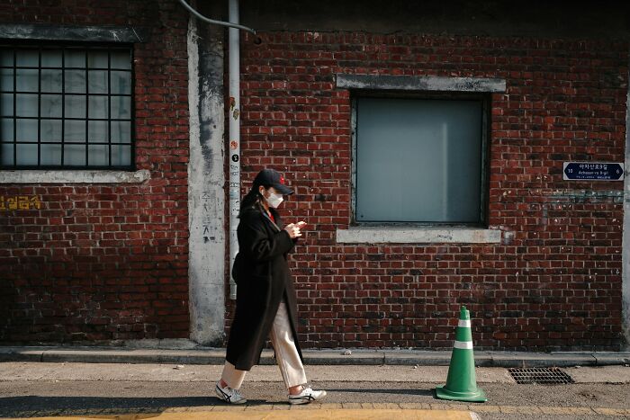 Person wearing mask and walking past brick wall, illustrating daily dangers you might not realize exposing yourself to.