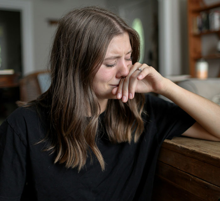 Young woman upset and crying indoors, symbolizing tension between MIL and DIL in a family conflict scenario.