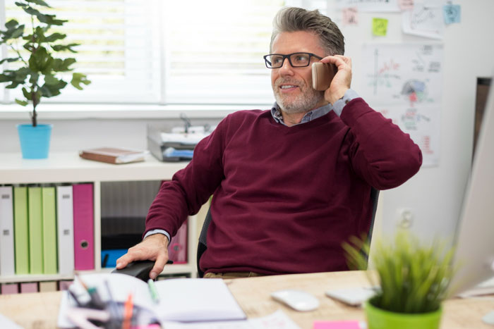 Man in glasses talking on phone in office, representing school principal handling autistic kid exclusion issue.