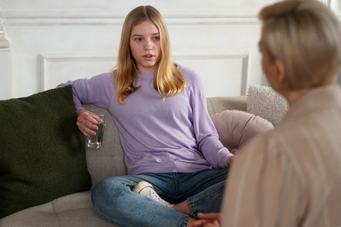 Teenage daughter sitting on couch holding a glass, talking to an older woman about a wedding dress dispute with her mom. Teenage daughter sitting on couch holding a glass, talking to an older woman about a wedding dress dispute with her mom.