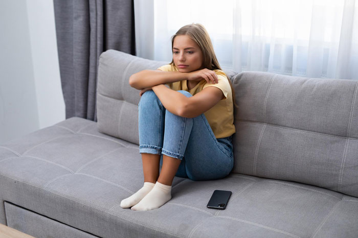 Young woman sitting on a couch looking trapped and sad, struggling with caring for autistic brother and school commitments