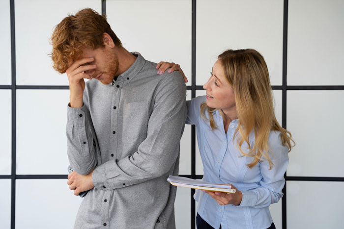 Male employee stressed while female coworker talks, illustrating coworkers trying to shame guy into donating PTO at work.