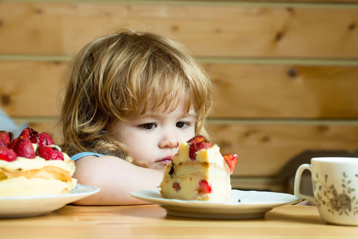 Little girl refusing to eat a slice of strawberry cake, showing reluctance and hesitation at the table.