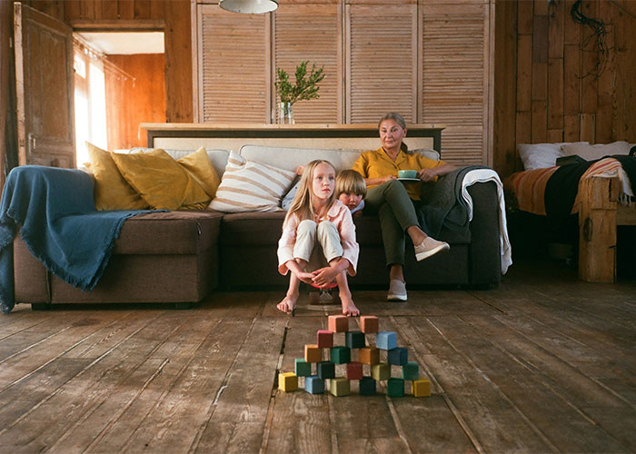 Woman and children sitting in living room with wooden blocks, illustrating neighbor conflict and child care challenges at night.