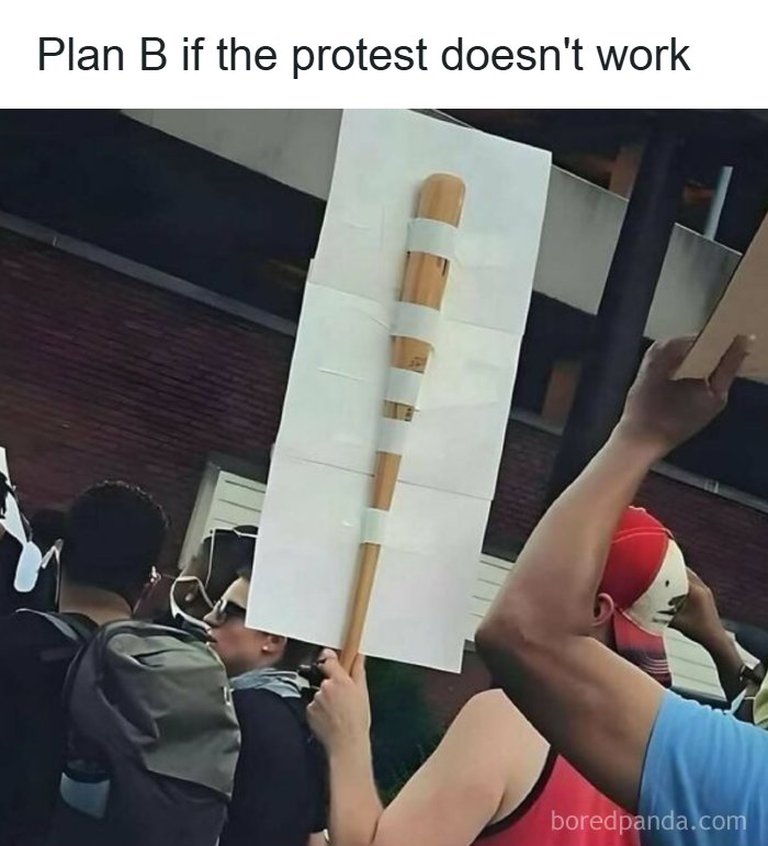 Protester holding a sign with a taped bat illustration, capturing humor in reality with memes about handling challenges.