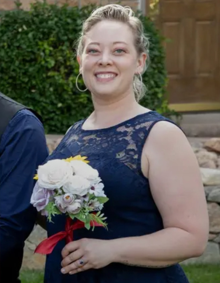 Woman holding bouquet outdoors, smiling and wearing a navy lace dress, representing autopsy released by Renee Good&rsquo;s family.