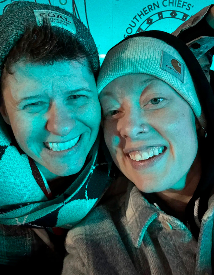 Two people smiling closely together wearing winter hats and jackets, related to Renee Good&rsquo;s wife and fatal ICE incident.
