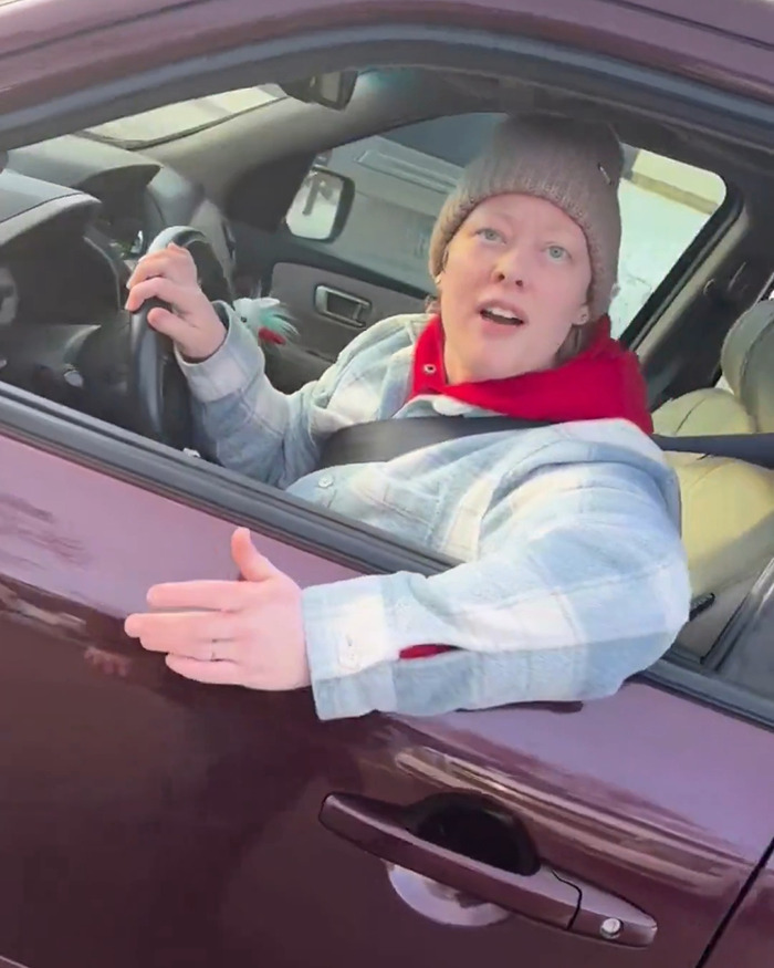 Person in a car wearing a beanie and red hoodie with arm extended, related to newly released ICE video context.