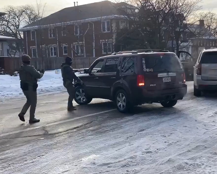 Two law enforcement officers approach a black SUV on a snowy street related to ICE video and fatal shooting context.