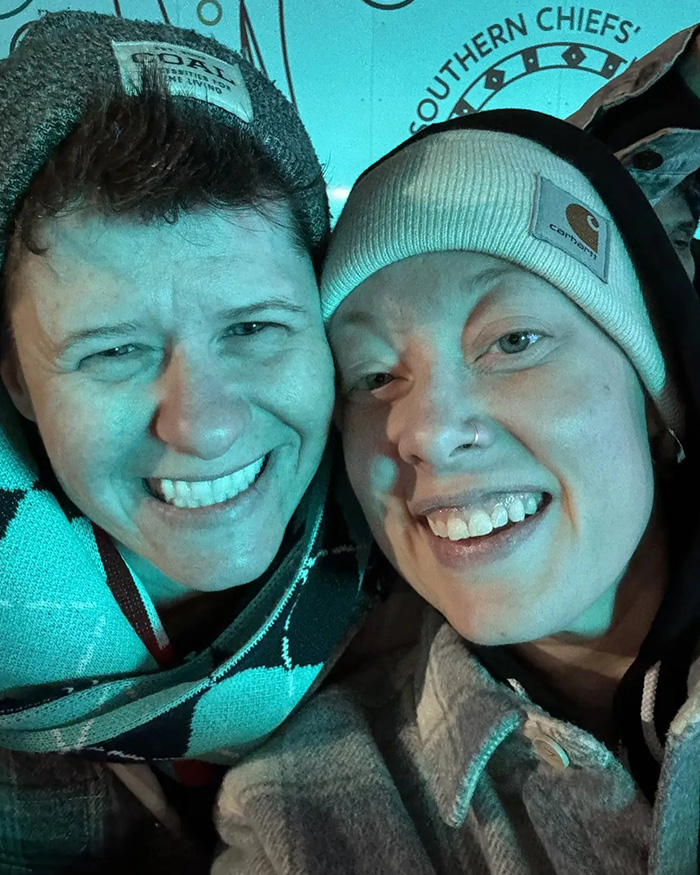 Two people smiling closely, both wearing beanies, illustrating context related to newly released ICE video.