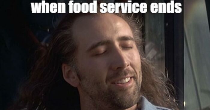 Man with long hair smiling contentedly in a restaurant setting, relatable moment for restaurant workers after food service ends.