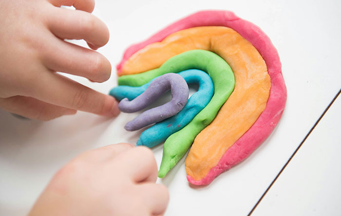 Child's hands shaping colorful rainbow clay, illustrating creative play and the joy of delivering glorious revenge.