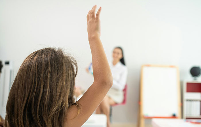 Child raising hand in classroom while teacher watches, capturing a moment of confident and victorious revenge.