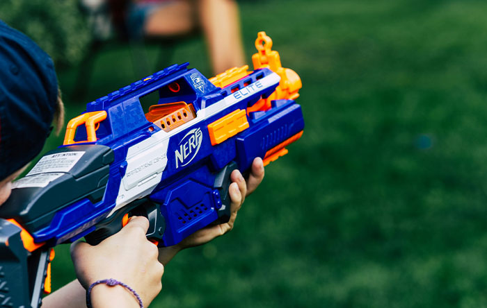 Child aiming a Nerf toy gun outdoors, capturing the playful moment of delivering glorious revenge with a foam dart.