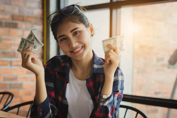 Young woman smiling indoors holding cash, illustrating rich people norms and insights on wealth and the 1 percent.