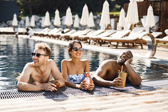 Three friends relaxing in a luxury pool with drinks, illustrating rich people norms and lifestyle insights from the 1 percent.