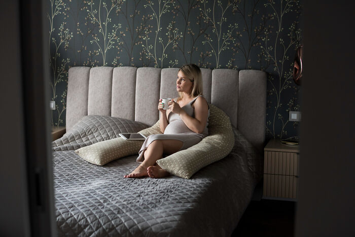 Woman relaxing on bed with cup in hand in a modern bedroom, illustrating rich people norms and lifestyle insights.