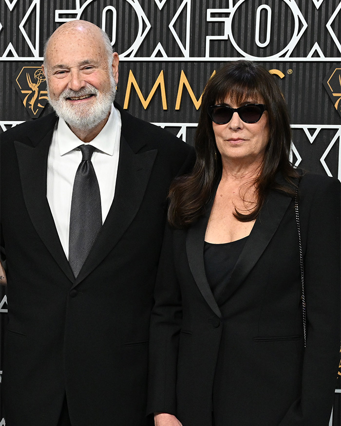 Man with white beard and woman in sunglasses in black formal attire at awards backdrop Man with white beard and woman in sunglasses in black formal attire at awards backdrop