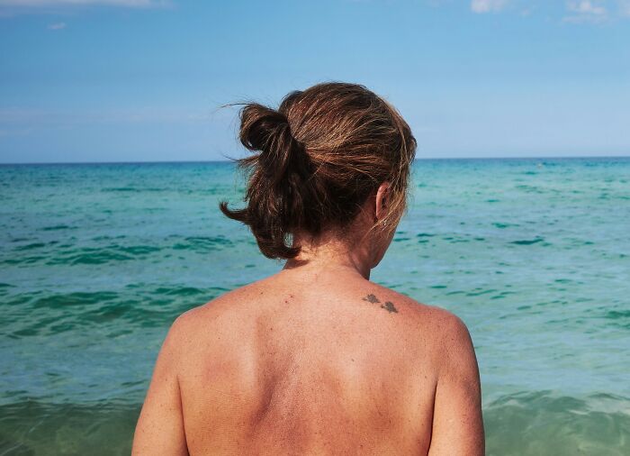 Person with a small tattoo on their back facing the ocean, illustrating cultural differences in what is considered normal or offensive.