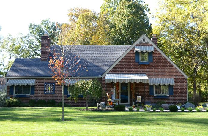 Brick house with a large lawn and striped awnings, representing common overrated adult goals like homeownership.