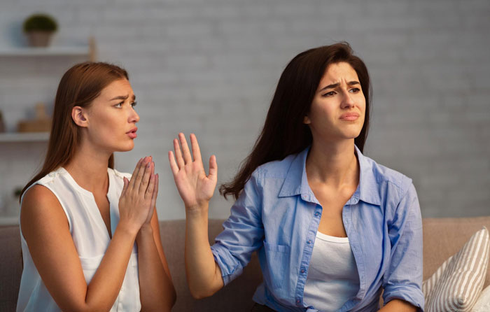 Two women having a tense conversation on a couch, portraying roommate boyfriend vacation drama emotions.