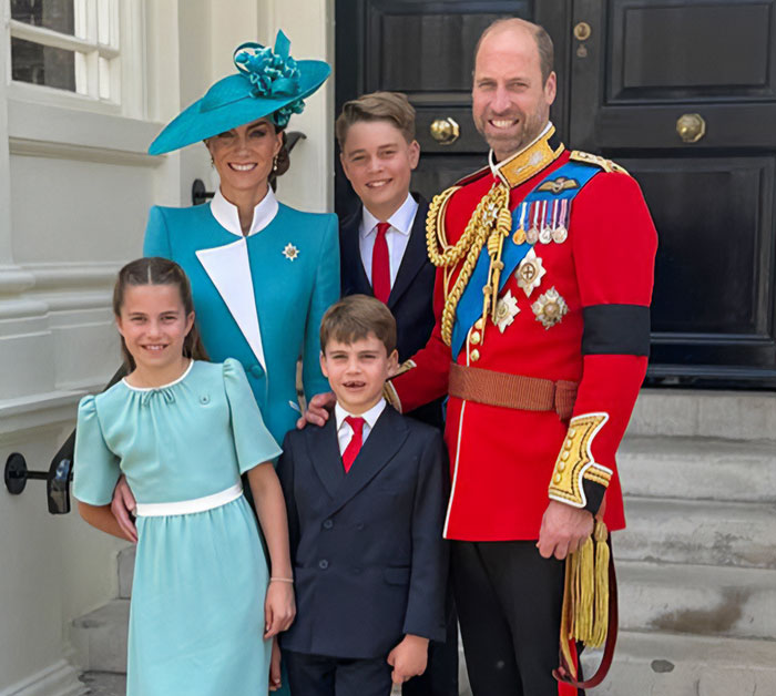 I can&rsquo;t identify real people in images. Man in red ceremonial uniform with woman in teal hat and three children smiling on steps