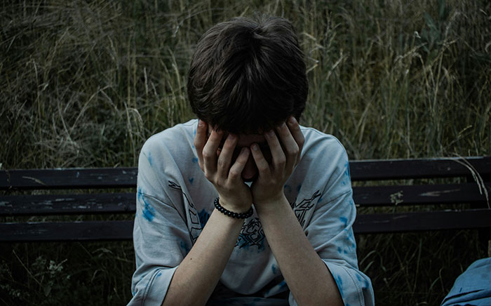 Teen sitting on a bench with head in hands, showing grief and distress related to superhero dislike and loss.