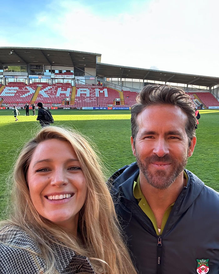 Ryan Reynolds smiling with a woman on a football field, linked to his legal battle and texts exposure.