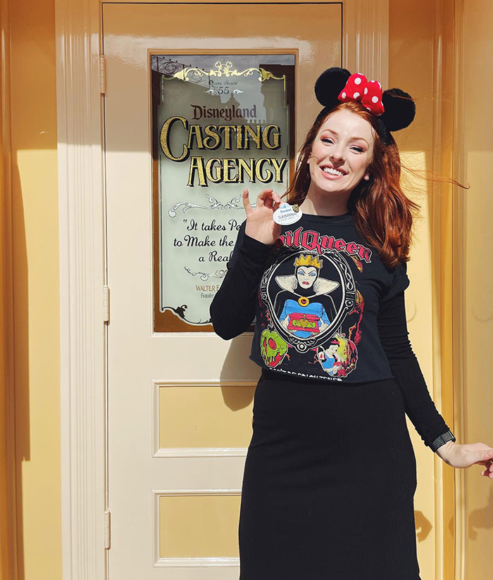 Young woman wearing Evil Queen shirt and Minnie ears smiling outside Disneyland Casting Agency, viral Evil Queen revealing her identity after firing.