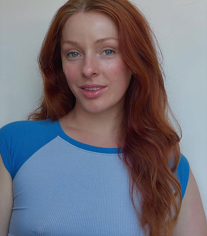 Red-haired woman smiling softly in a blue shirt, representing the viral Evil Queen revealing her identity after Disneyland firing.