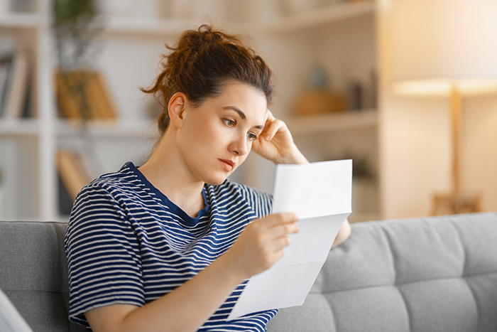 Woman sitting on couch reading husband's note, looking confused and upset, capturing emotional reaction in home setting.