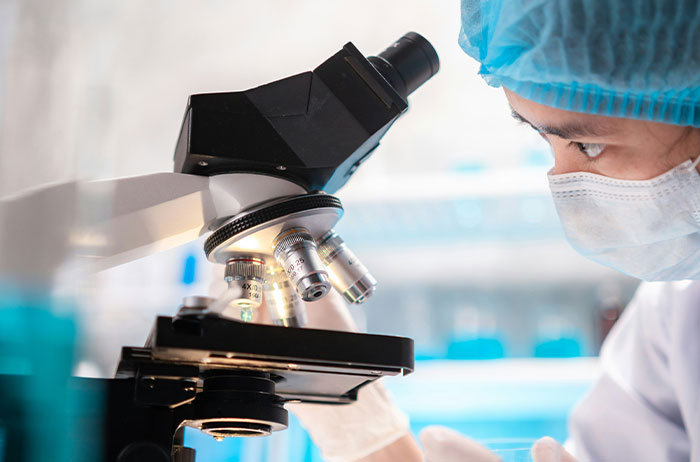 Saw Images On Google scientist in mask and surgical cap examining slide under microscope in bright lab.