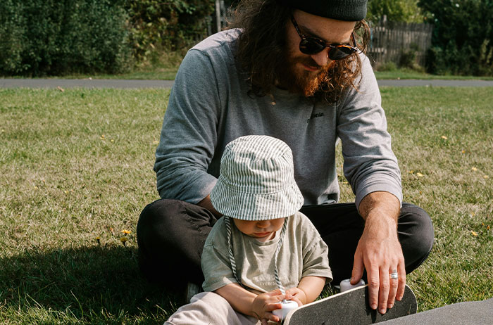 Father and toddler sitting on grass with skateboard, candid scene suggesting saw images on google