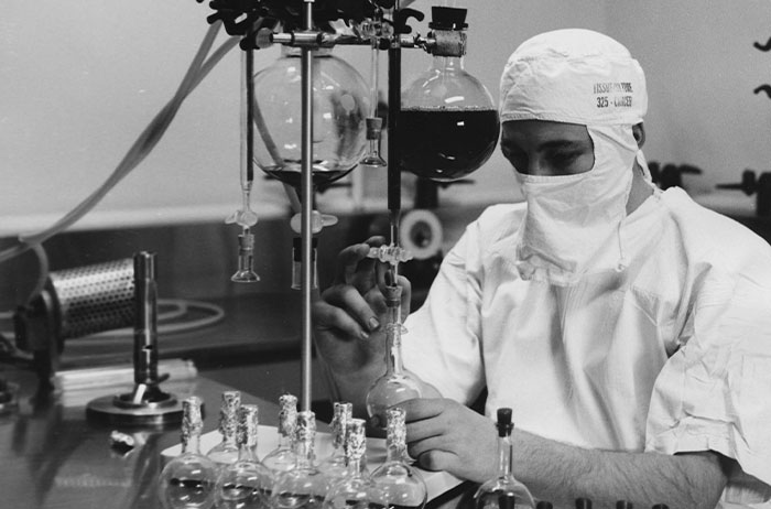 Lab technician in protective suit and mask handling glass flasks in sterile laboratory, traumatized imagery