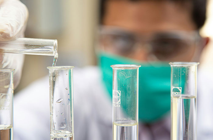 Lab technician wearing mask pouring liquid into test tubes, saw images on Google