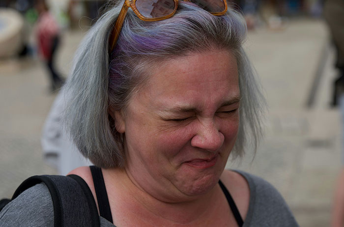 Woman wincing in disgust, reacting as if she saw images on Google, gray hair, sunglasses on head, crowded street background.