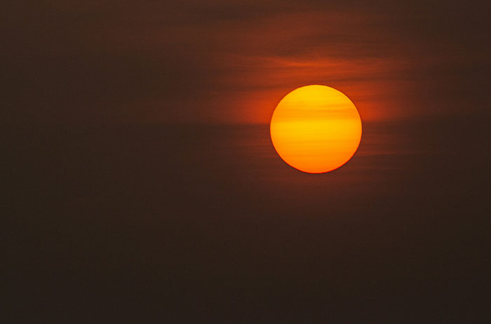 Hazy orange sun at sunset against a dark sky, haunting scene, traumatized