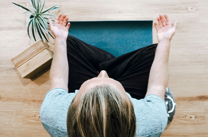 Overhead view of a person meditating on a yoga mat with palms up beside a plant and blocks, Saw Images On Google