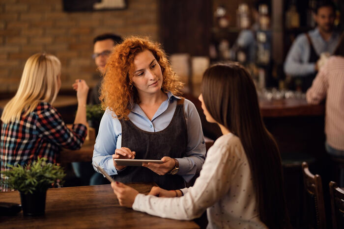 Waitress with red curly hair taking order from customer, illustrating a moment of meeting a high school bully as adults.