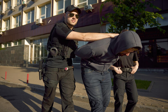 Police officer detaining a man in a hoodie on a city street, illustrating karma meeting a high school bully as an adult.