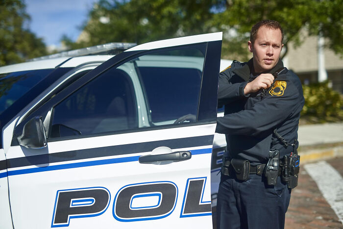 Police officer standing next to patrol car, symbolizing karma moments when people met their high school bully as adults.