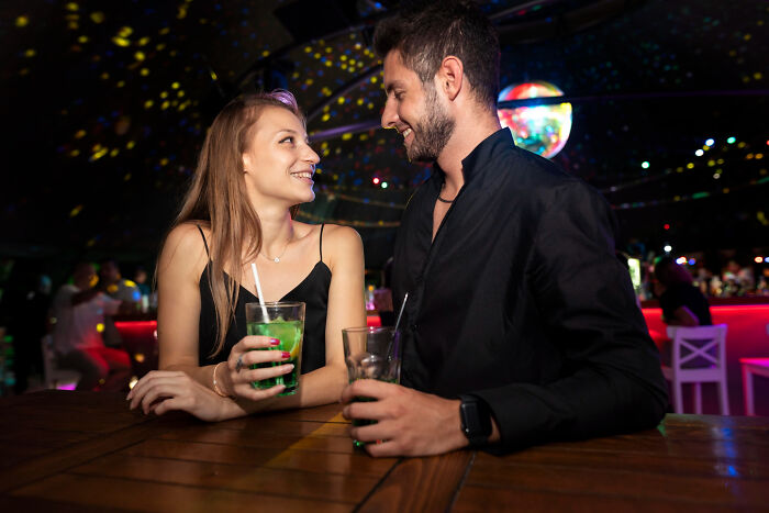 Young man and woman smiling and holding drinks at a bar, illustrating people meeting their high school bully as adults.