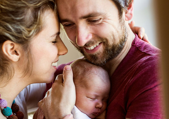 Happy couple holding their newborn baby close, sharing intimate moments and expressing love and protection.